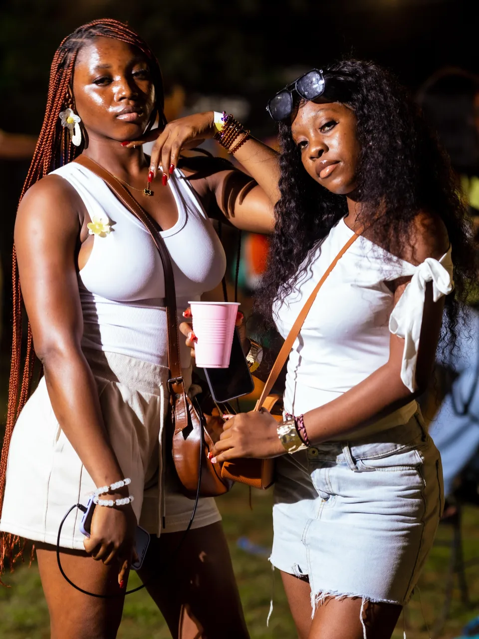 Two friends in white outfits posing together at an outdoor evening gathering