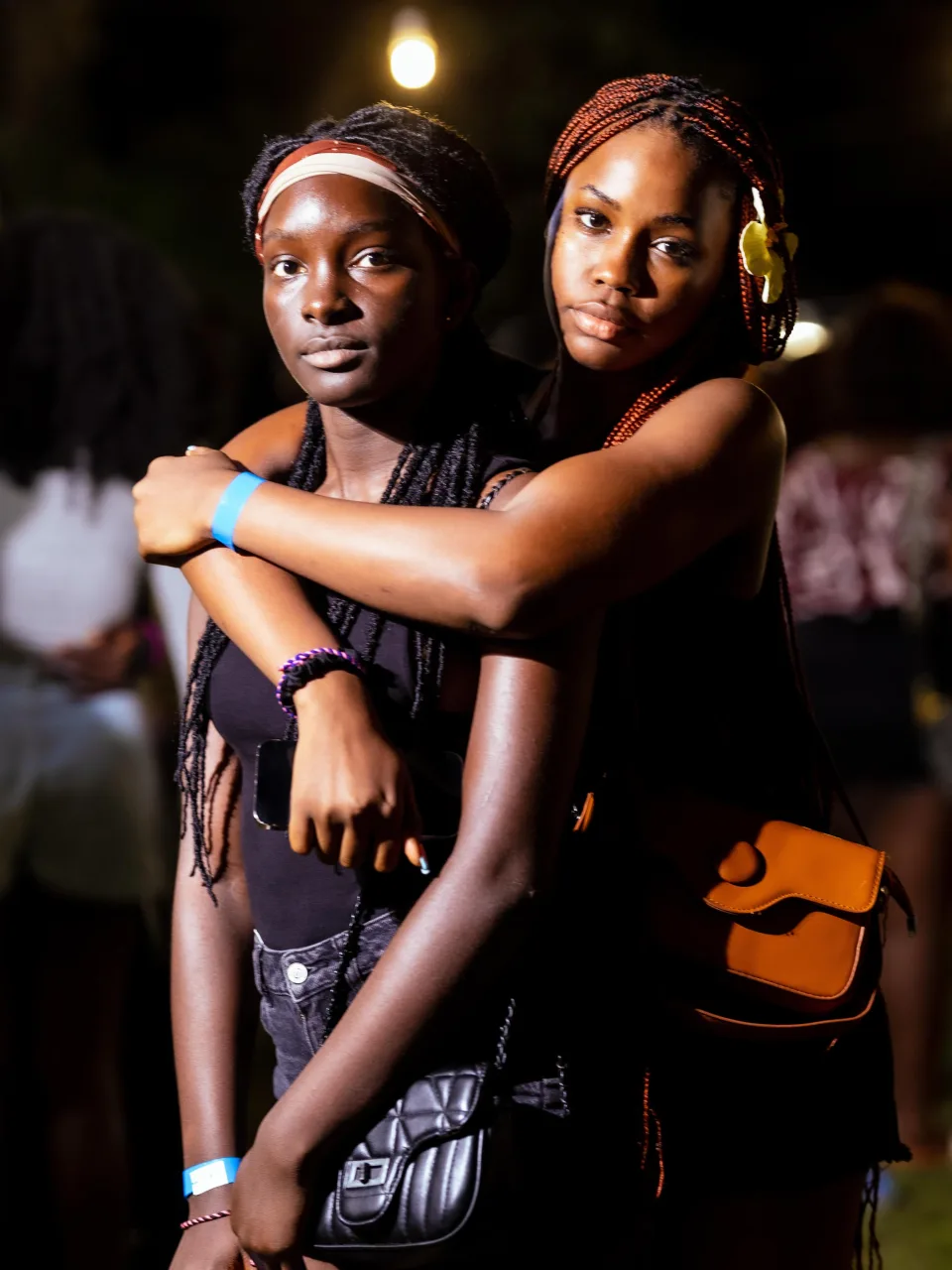 Two friends with blue event wristbands sharing a hug under the evening lights