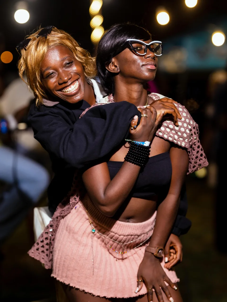 Two friends smiling and embracing beneath strings of lights at a Circles gathering